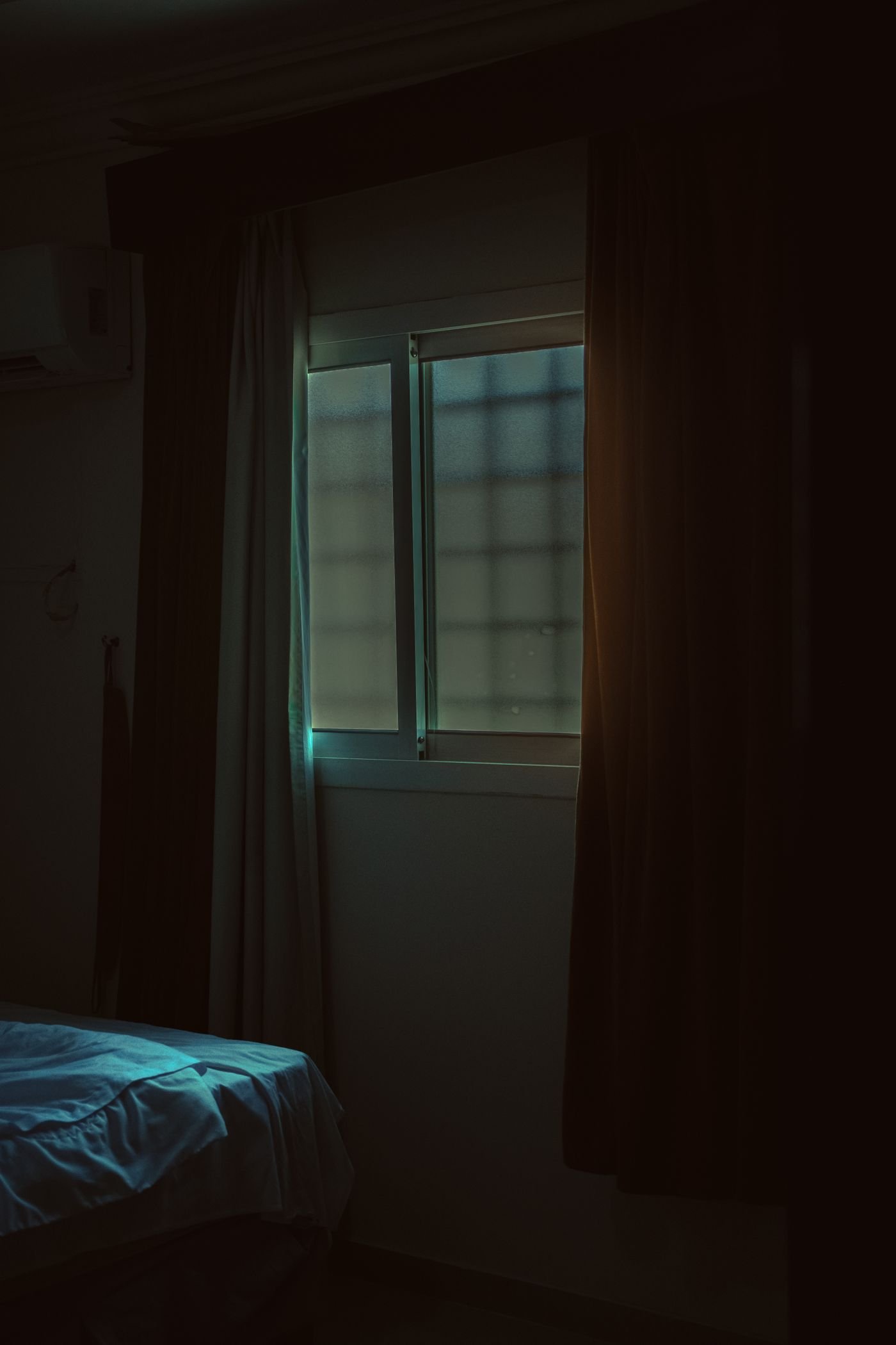 A dark bedroom with pale light coming through a window past a drawn curtain