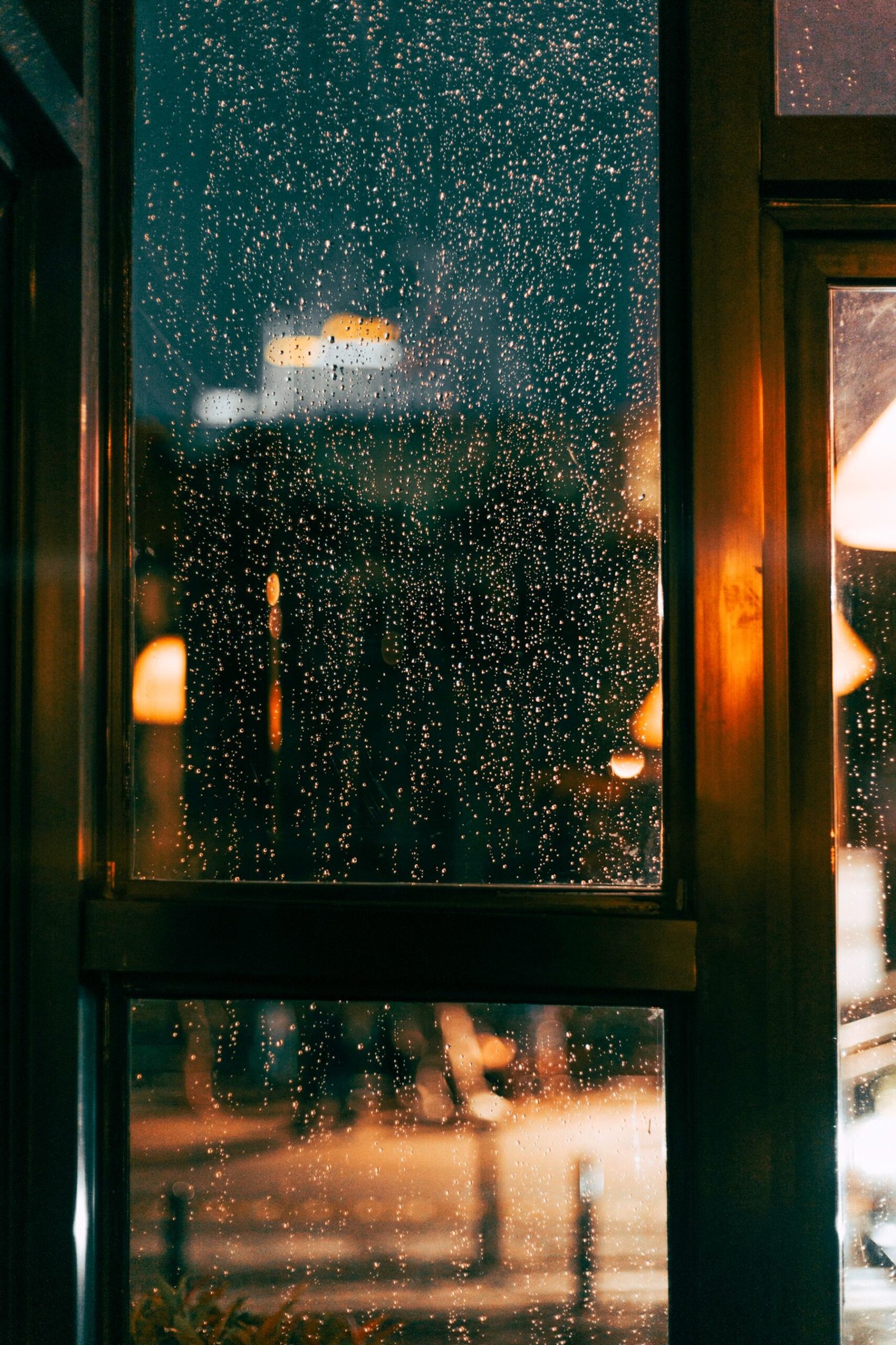 Rain running down a dark window pane at night, with warm amber street lights blurred behind it